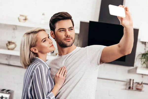 Bello fidanzato e attraente fidanzata prendendo selfie in cucina — Foto stock