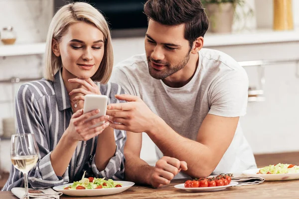 Enfoque selectivo de novio guapo y novia atractiva usando el teléfono inteligente - foto de stock