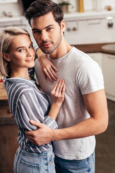 Guapo novio y atractiva novia abrazando y mirando a la cámara - foto de stock