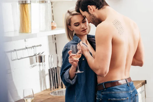 Enfoque selectivo de novia atractiva y novio guapo sosteniendo copa de vino y abrazos en la cocina - foto de stock