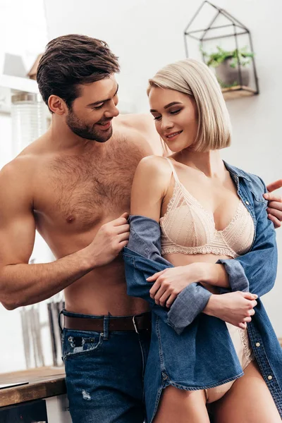 Enfoque selectivo de novia atractiva y novio guapo abrazando y sonriendo en la cocina - foto de stock