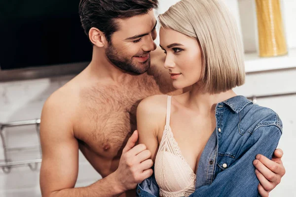 Enfoque selectivo de novia atractiva y novio guapo abrazando y sonriendo en la cocina — Stock Photo