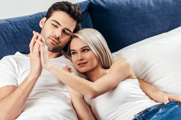 Selective focus of attractive girlfriend and handsome boyfriend laying and holding hands — Stock Photo