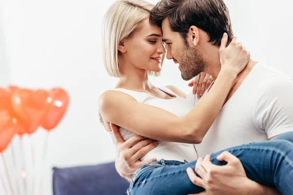 Selective focus of attractive girlfriend and handsome boyfriend holding and kissing at home on Valentines day — Stock Photo