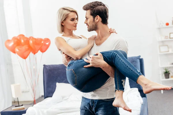 Selective focus of handsome boyfriend holding attractive girlfriend at bedroom on Valentines day — Stock Photo