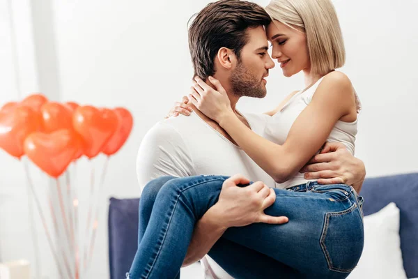 Enfoque selectivo de novio guapo sosteniendo novia atractiva en el dormitorio en el día de San Valentín - foto de stock