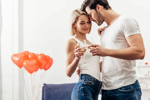 Selective focus of attractive girlfriend and handsome boyfriend smiling and holding wine glasses on Valentines day — Stock Photo