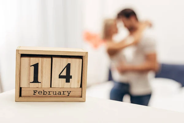 Enfoque selectivo del calendario de madera con 14 letras de febrero y pareja joven en el fondo en el día de San Valentín - foto de stock
