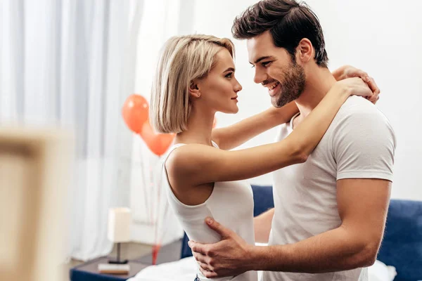 Selective focus of attractive girlfriend and handsome boyfriend hugging in bedroom on Valentine's day — Stock Photo