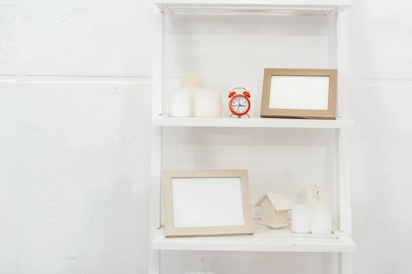 Étagères avec horloge rouge, cadres en bois et bougies sur fond blanc — Photo de stock