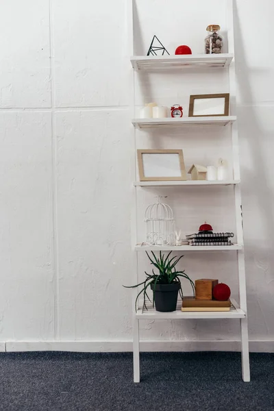 Shelves with red clock, wooden frameworks, plant, books, bottle with seashells and candles on white background — Stock Photo