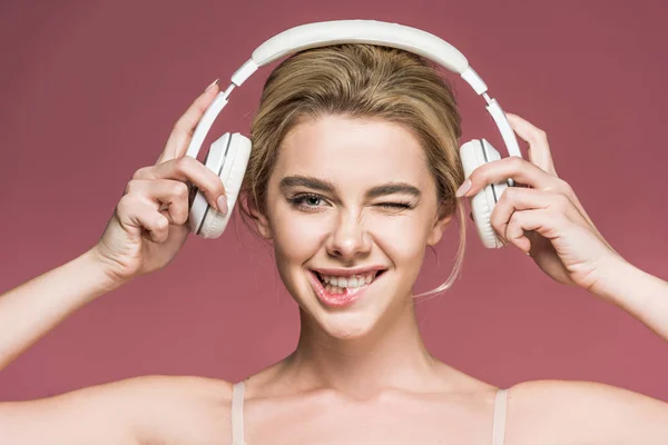 Belle fille souriante cligner des yeux et écouter de la musique avec écouteurs, isolé sur rose — Photo de stock