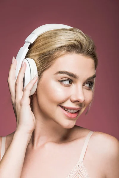 Chica rubia feliz escuchando música con auriculares, aislado en rosa - foto de stock