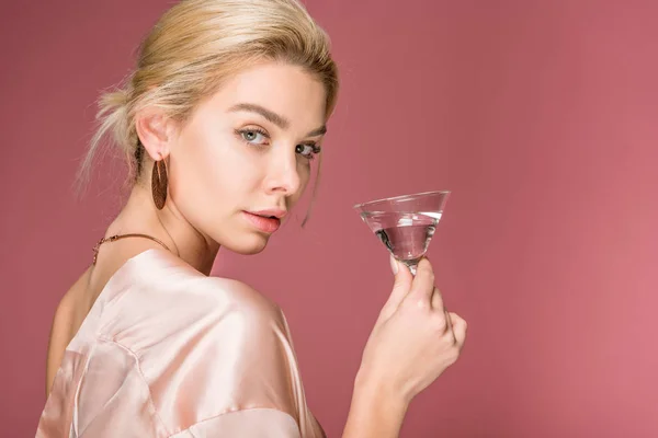 Bella ragazza elegante in abito di seta in possesso di bicchiere da cocktail, isolato su rosa — Foto stock