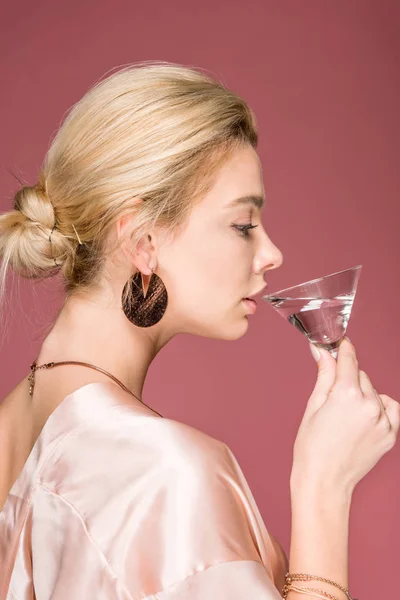 Vista lateral de atractiva chica elegante en traje de seda beber cóctel, aislado en rosa — Stock Photo