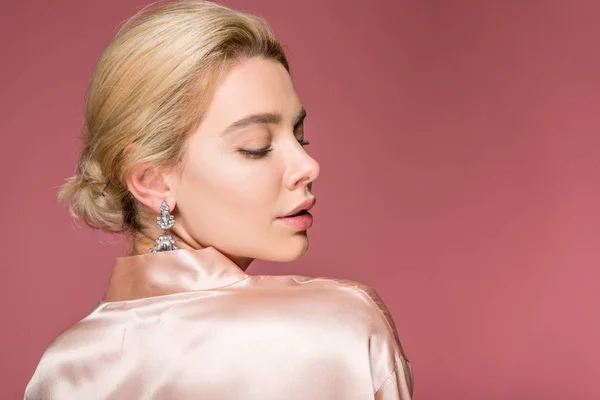 Schöne blonde Frau posiert in Ohrringen und Seidenmantel, isoliert auf rosa — Stockfoto