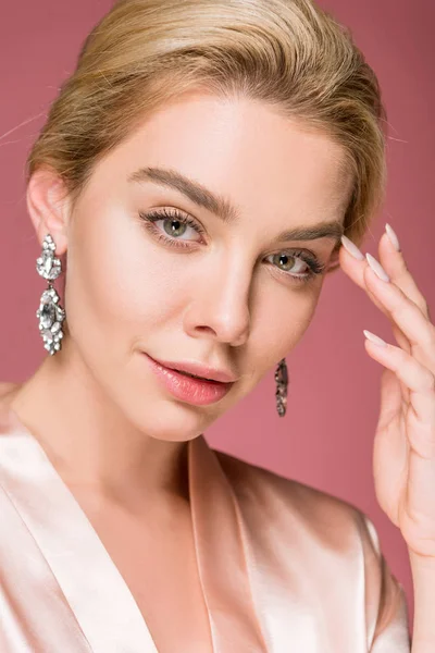 Portrait of attractive blonde woman posing in earrings and silk robe, isolated on pink — Stock Photo