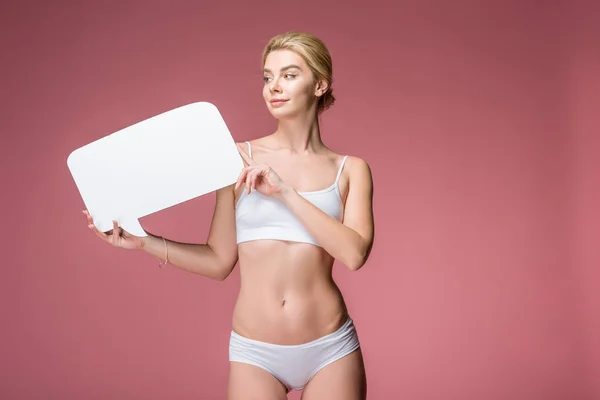 Atractiva mujer delgada en ropa interior blanca posando con la burbuja del habla vacía, aislado en rosa - foto de stock