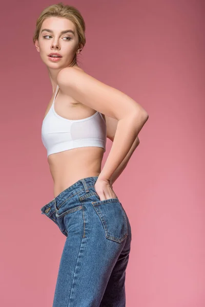Schöne schlanke Frau posiert in Jeans und weißem BH, isoliert auf rosa — Stockfoto