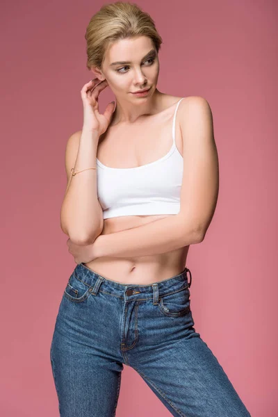 Красива блондинка позує в джинсах і білому бюстгальтері, ізольована на рожевому — стокове фото
