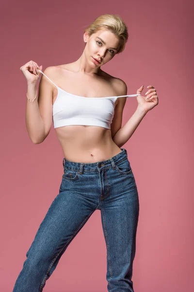 Beautiful young woman posing in jeans and white bra, isolated on pink — Stock Photo