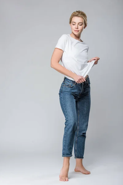 Красива усміхнена жінка в джинсах роздягається ізольовано на сірому — стокове фото