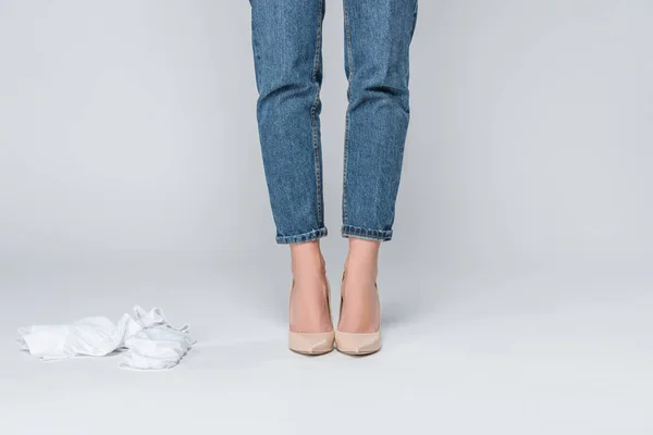 Vue recadrée de la femme en jeans et talons hauts se déshabillant isolé sur gris — Photo de stock