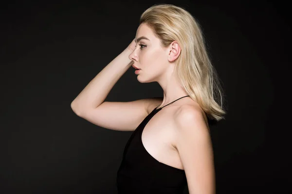 Seitenansicht des blonden Mädchens im schwarzen Kleid posiert isoliert auf schwarz — Stockfoto