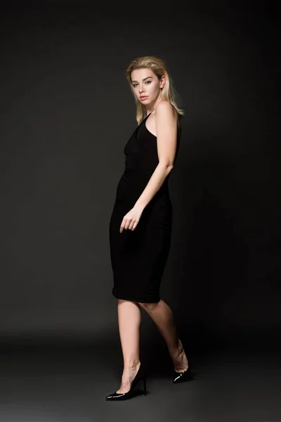 Beautiful young woman in elegant black dress posing on black — Stock Photo