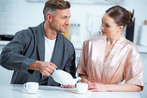 Messa a fuoco selettiva di bella coppia adulta in accappatoi prendere il tè in cucina — Foto stock