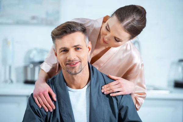 Beautiful woman in robe embracing smiling man in kitchen — Stock Photo