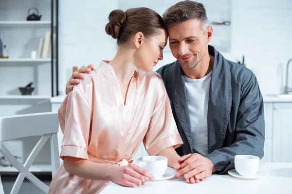 Beau couple adulte en peignoirs ayant le thé dans la cuisine — Photo de stock