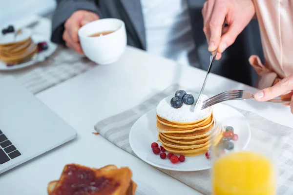 Vista parcial de la mujer cortando panqueques durante el desayuno en la cocina - foto de stock