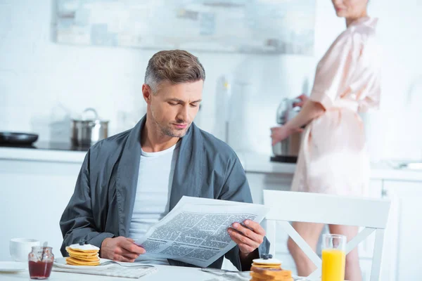 Bell'uomo che legge il giornale durante la colazione in cucina — Foto stock