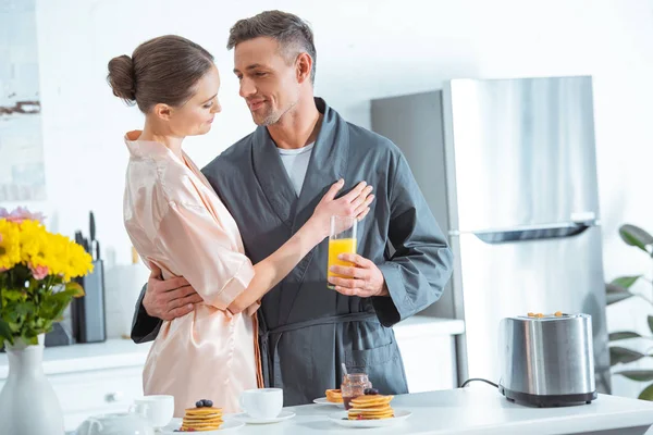 Schöne Frau in Robe umarmt Mann beim Frühstück in der Küche — Stockfoto