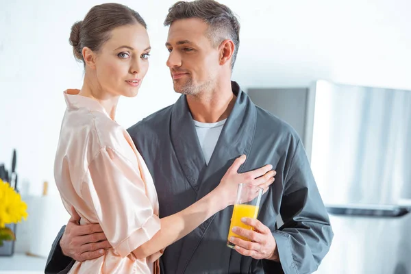 Selective focus of beautiful woman in robe embracing man during breakfast in kitchen — Stock Photo