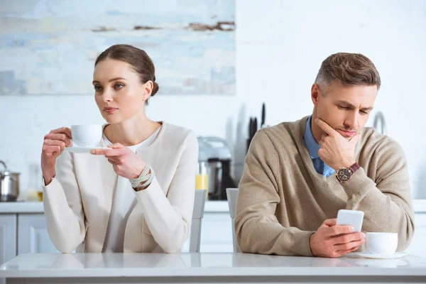 Man using smartphone and ignoring upset woman during breakfast in kitchen — Stock Photo