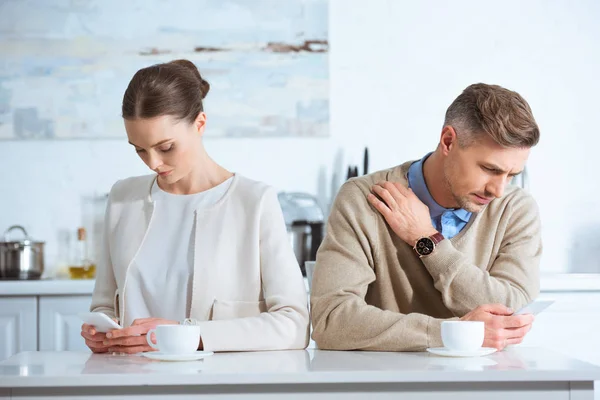 Coppia adulta seduta a tavola, utilizzando smartphone e ignorandosi a vicenda durante la colazione — Foto stock