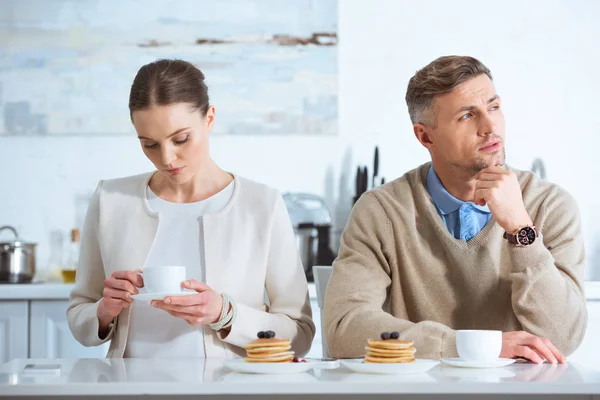 Selective focus of adult couple sitting at table and ignoring each other during breakfast in morning — Stock Photo