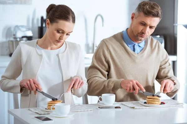 Расстроенная женщина сидит за столом и игнорирует мужчину во время завтрака утром — стоковое фото