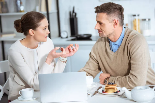 Доросла пара використовує ноутбук і розмовляє під час сніданку вранці — стокове фото