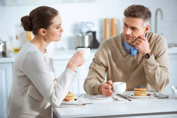 Selective focus of dissatisfied adult couple sitting at table while having breakfast in morning — Stock Photo