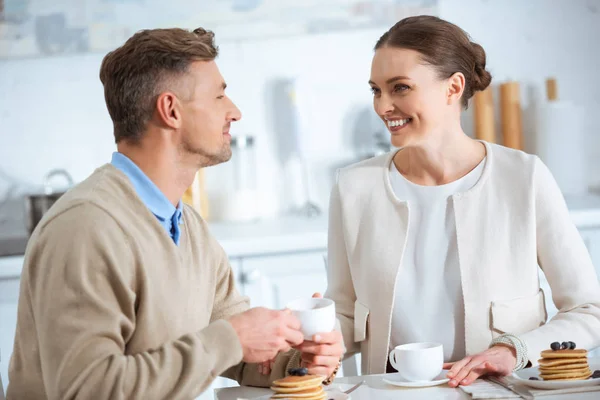 Красивая улыбающаяся пара смотрит друг на друга во время завтрака утром — стоковое фото