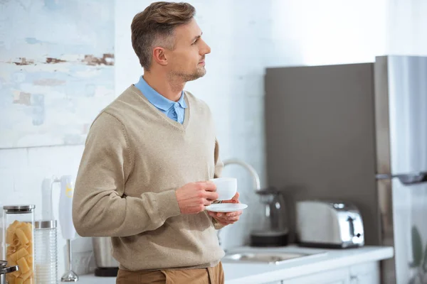 Handsome man in casual clothes holding coffee cup in kitchen — Stock Photo