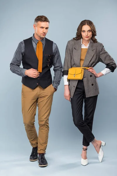 Stylisches Paar in formeller Kleidung, das vor grauem Hintergrund in die Kamera blickt — Stockfoto