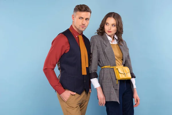 Hermosa pareja de moda en desgaste formal mirando hacia otro lado y posando aislado en azul - foto de stock