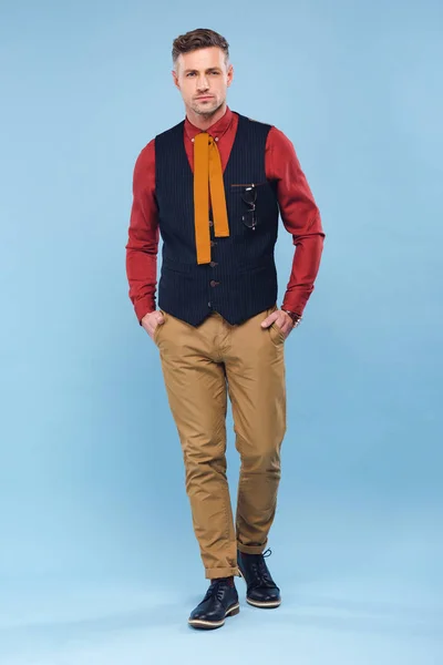 Schöner nachdenklicher stilvoller Mann in formeller Kleidung mit Händen in Taschen auf blauem Hintergrund — Stockfoto