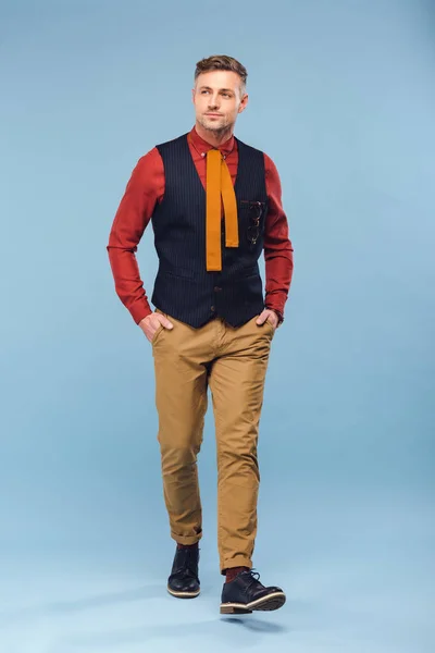 Hombre elegante guapo en ropa formal con las manos en los bolsillos sobre fondo azul - foto de stock