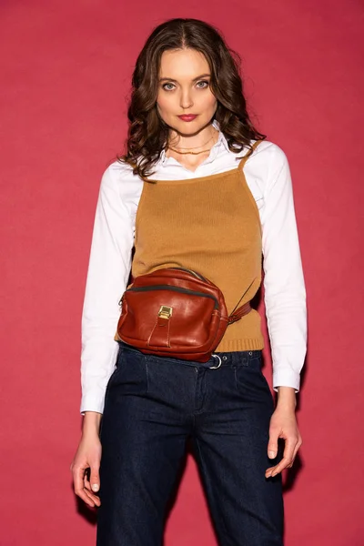 Belle femme élégante en tenue formelle avec sac en cuir posant sur fond rouge — Photo de stock