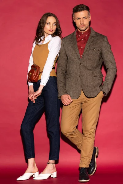 Atraente casal na moda em desgaste formal posando no fundo vermelho — Fotografia de Stock